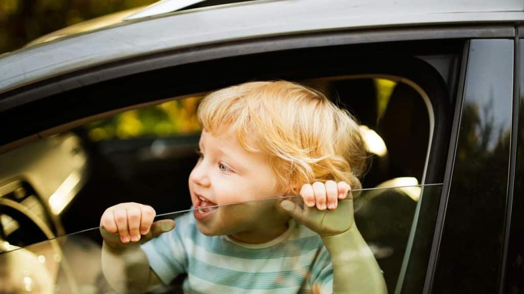 A smiling child leaning out of a car window.