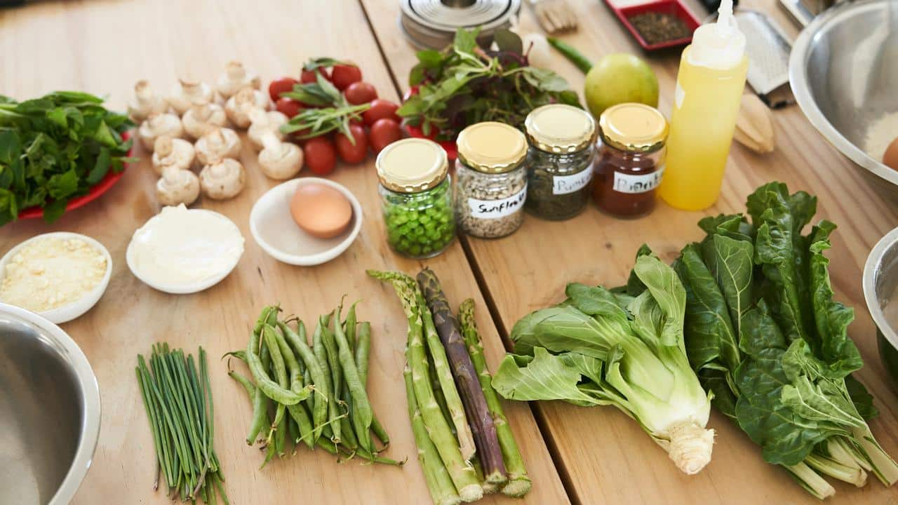 A table filled with fresh vegetables, herbs, eggs, cheese, and jars of ingredients.