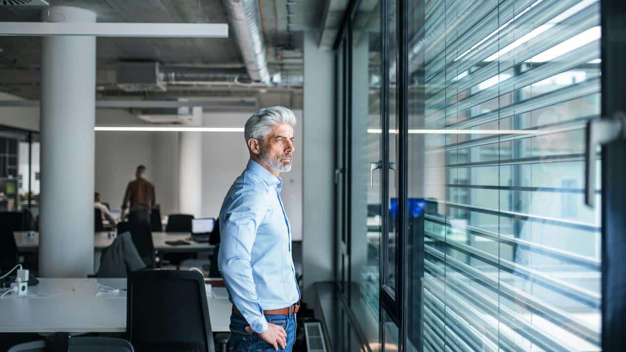 A man standing in an office, looking out the window.