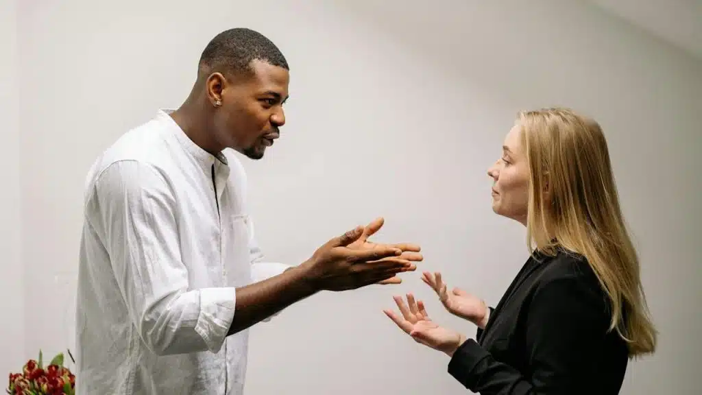 A man and woman face each other, gesturing with their hands as if in discussion.