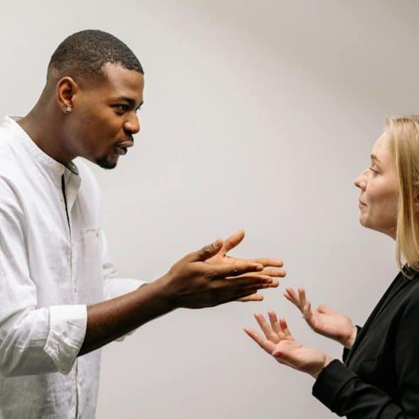 A man and woman face each other, gesturing with their hands as if in discussion.