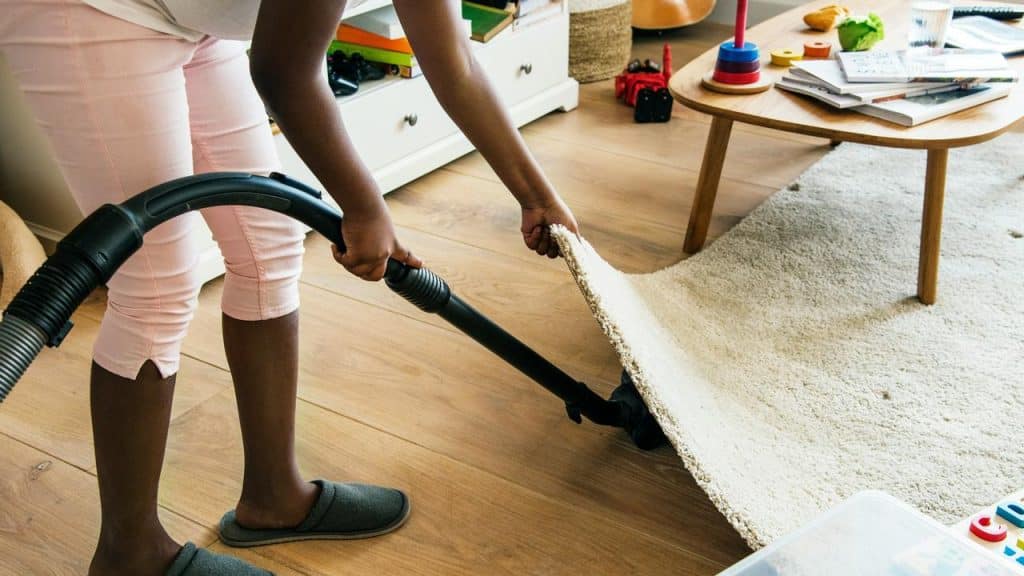 A person vacuuming under a rug in a living room.
