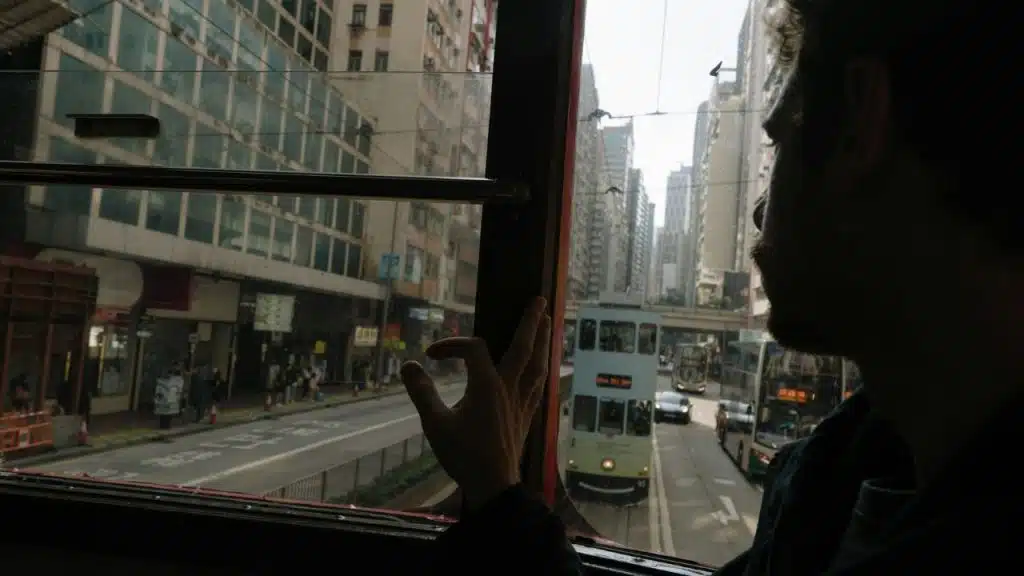 A man looks out a window at a city street with a double-decker tram below.
