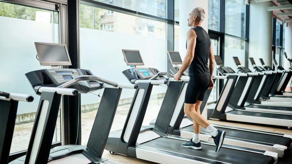 An older man walking on a treadmill in a gym.