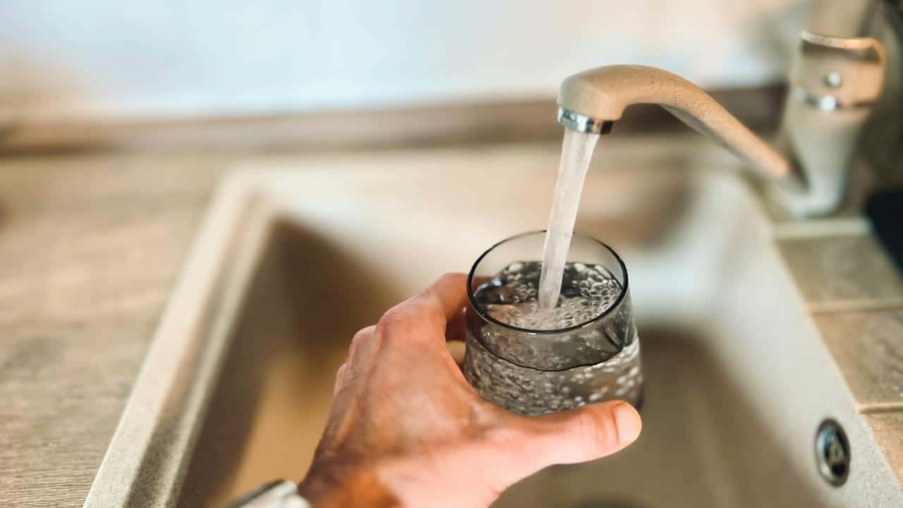 A hand filling a glass with water from a faucet.