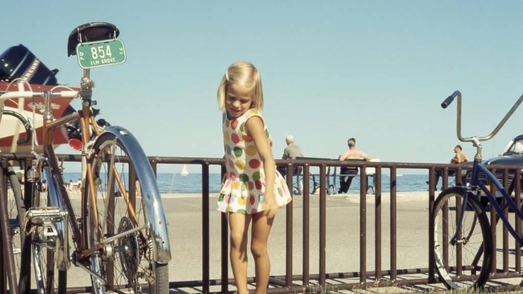A young girl in a polka dot dress standing by bikes near the beach.