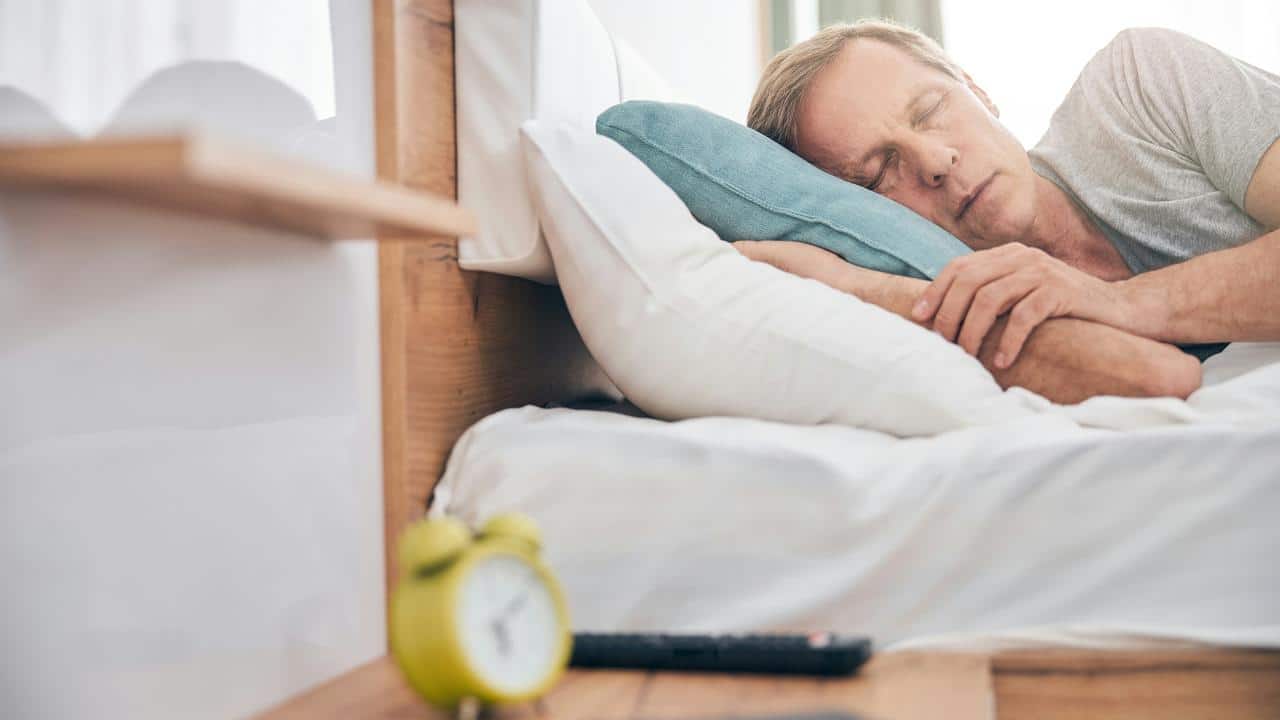 A man sleeps in bed with his arms tucked in.