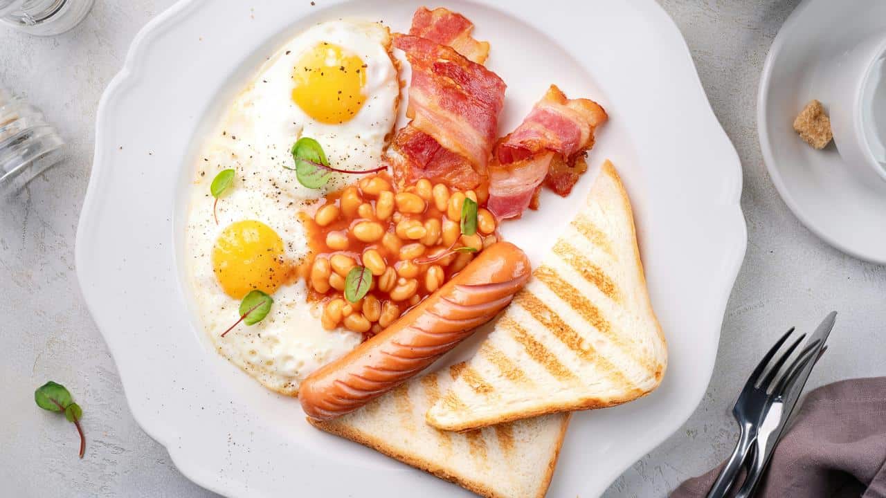 A breakfast plate with eggs, bacon, beans, sausage, and toast.