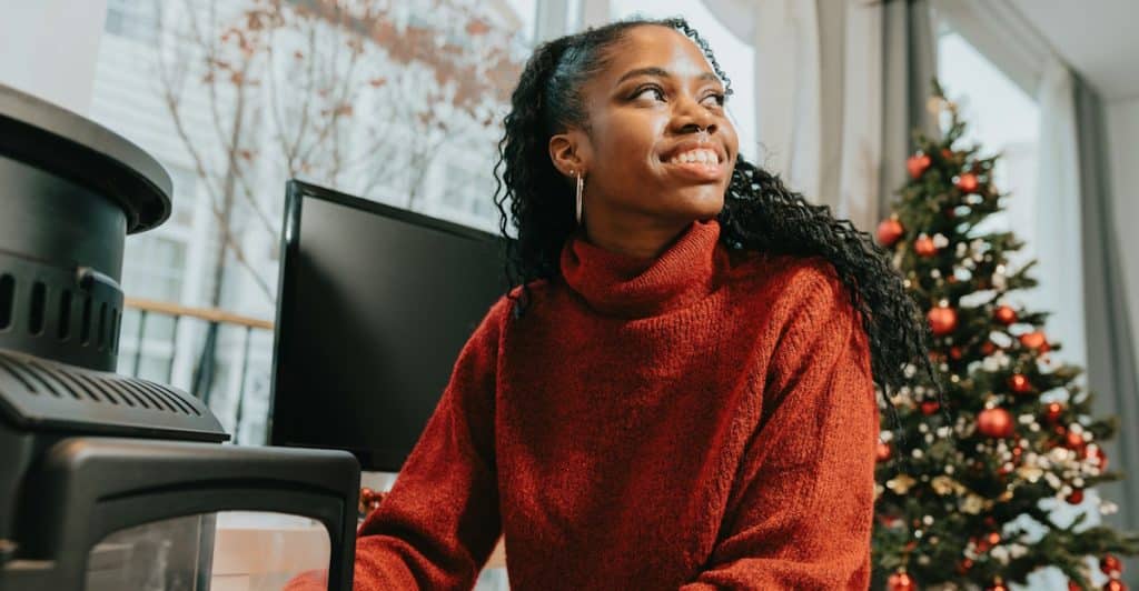 A woman in a red sweater smiles while sitting indoors near a Christmas tree.