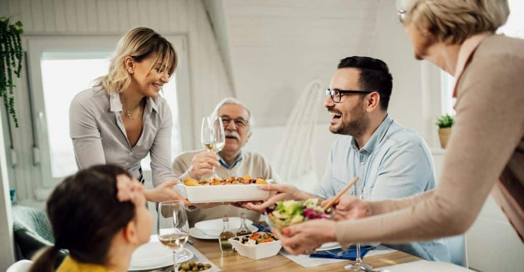 A family gathers around a table, smiling and sharing food during a meal.