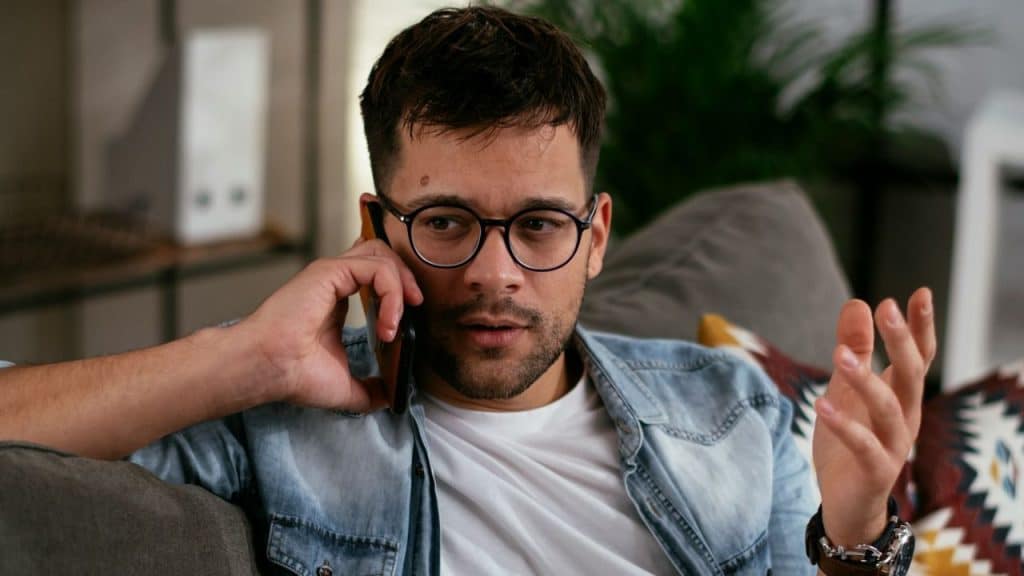 A man wearing glasses is having a tense phone conversation.