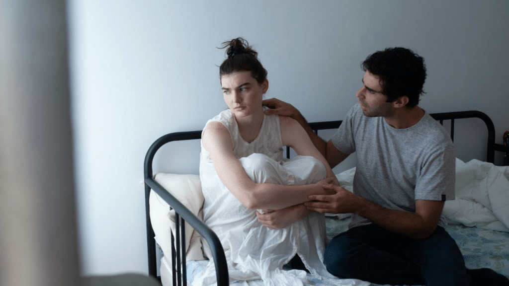 A calm man comforts an upset woman sitting on a bed.