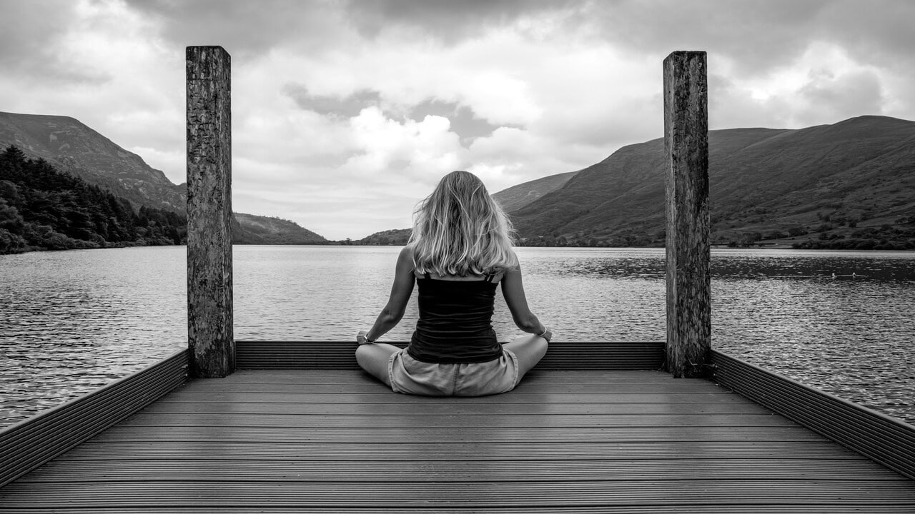 A woman meditating by a body of water.