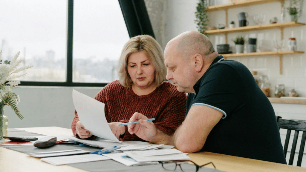 A serious-looking couple sits at a table, reviewing documents together.