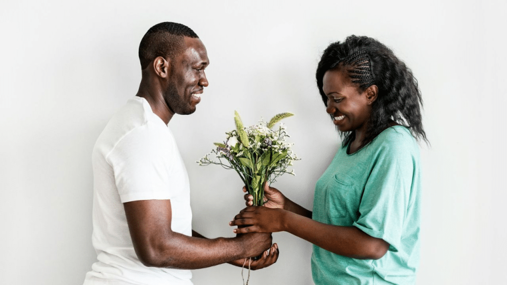 A man in a white shirt smiles at a woman as he hands her a bouquet of flowers. They are both smiling.