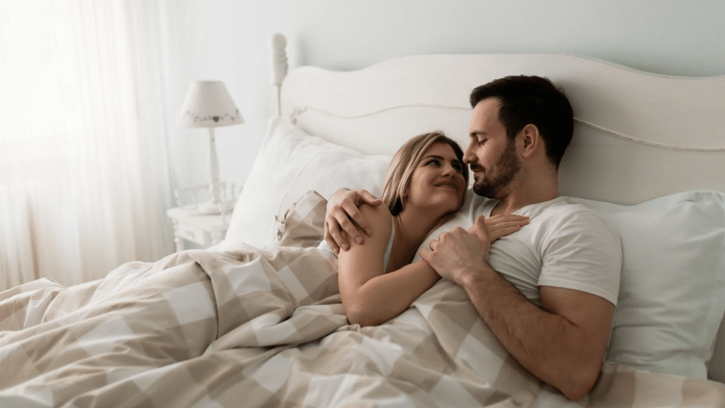 A smiling couple with heads together lies in bed, embracing.