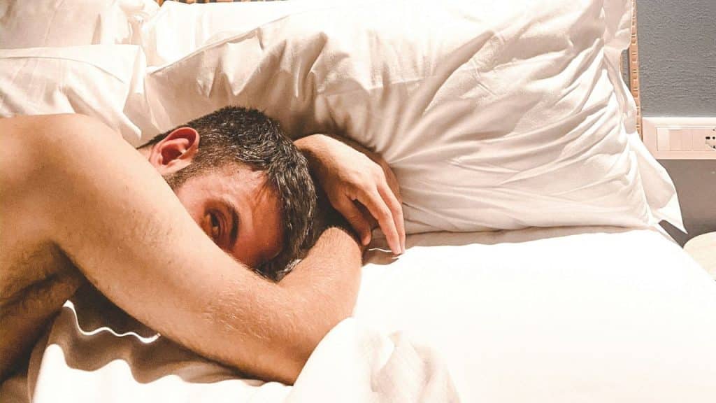 A man is lying face down on a bed, looking over his shoulder.