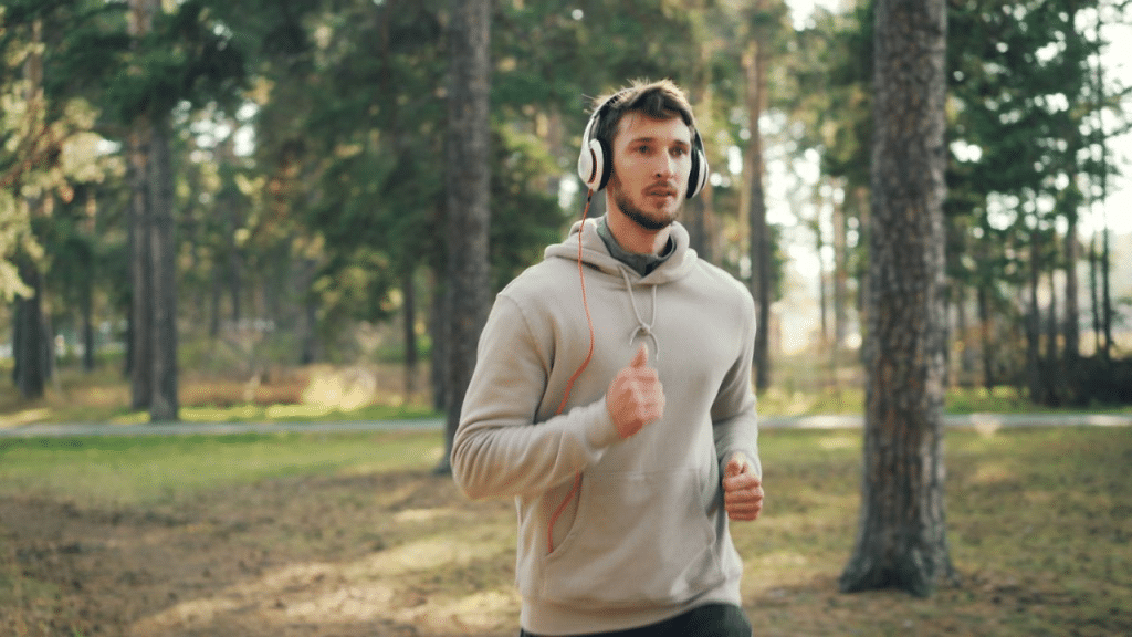A man wearing headphones runs on a trail through a forest.