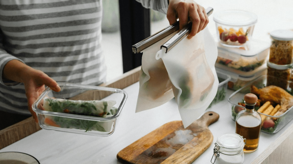 A person storing food in reusable containers and silicone bags on a kitchen counter.