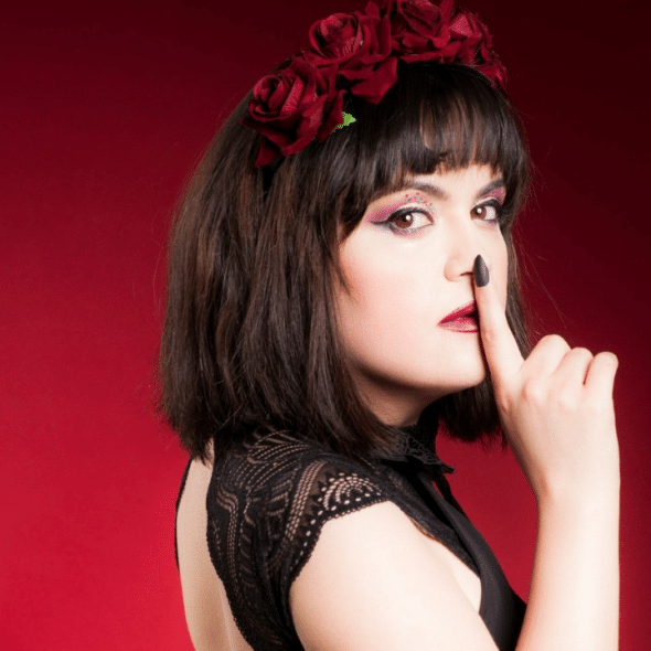 A woman in a lace top and a red rose headband holds a finger to her mouth.