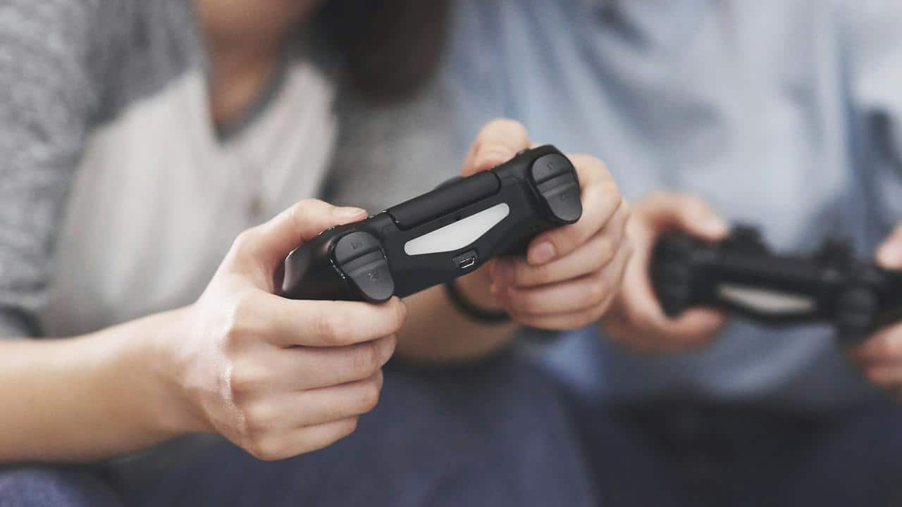 A close-up of two people holding video game controllers while playing.