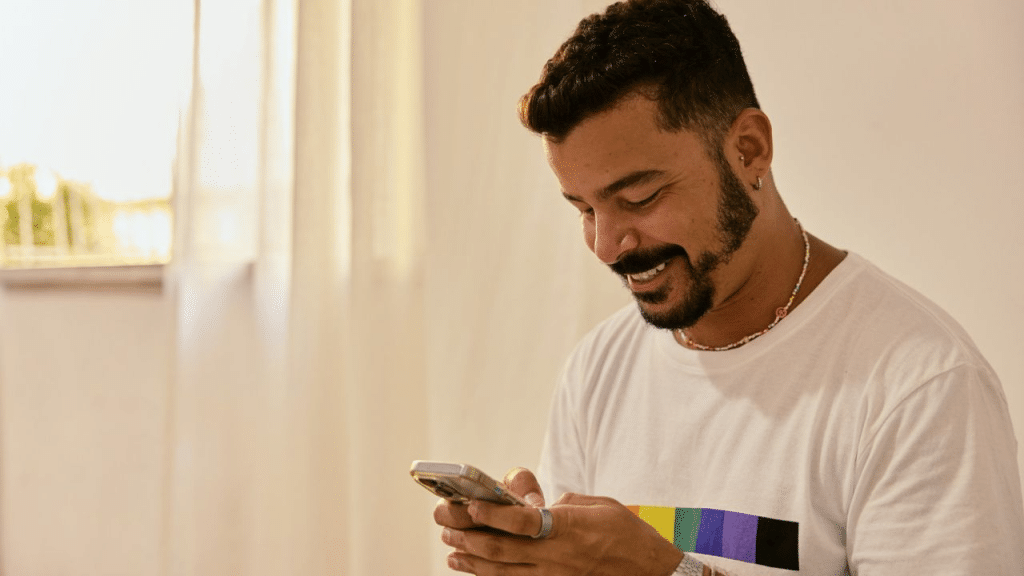 A smiling man with a beard and a necklace looks down at his phone.