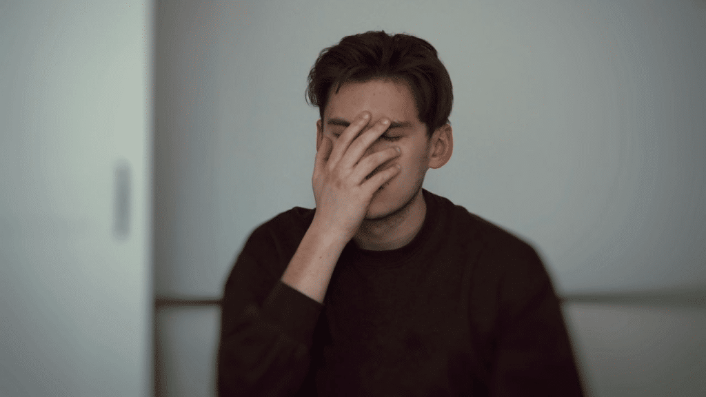 A man sits with his hand over his face, looking distraught.