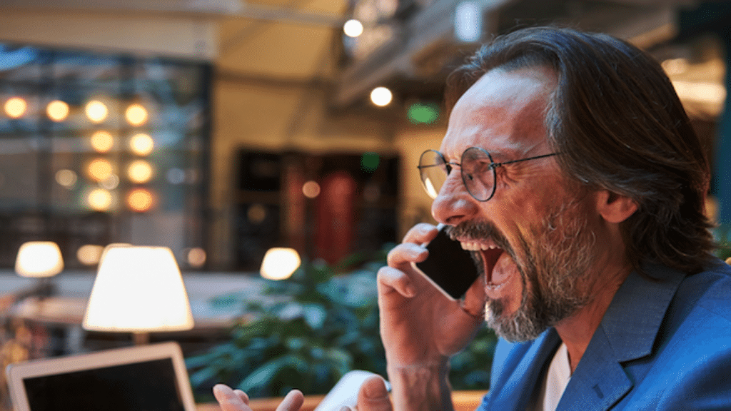 Angry man with glasses and a goatee shouting into a smartphone