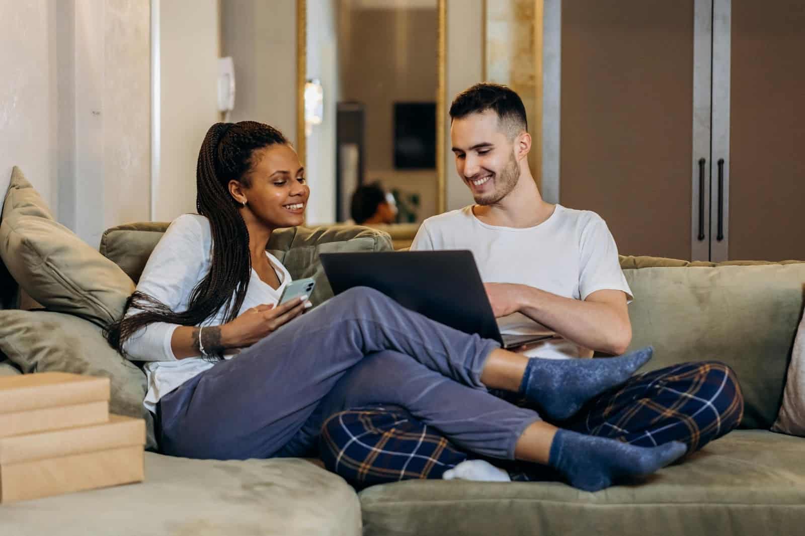 A man holding the laptop and a woman using a phone while watching.