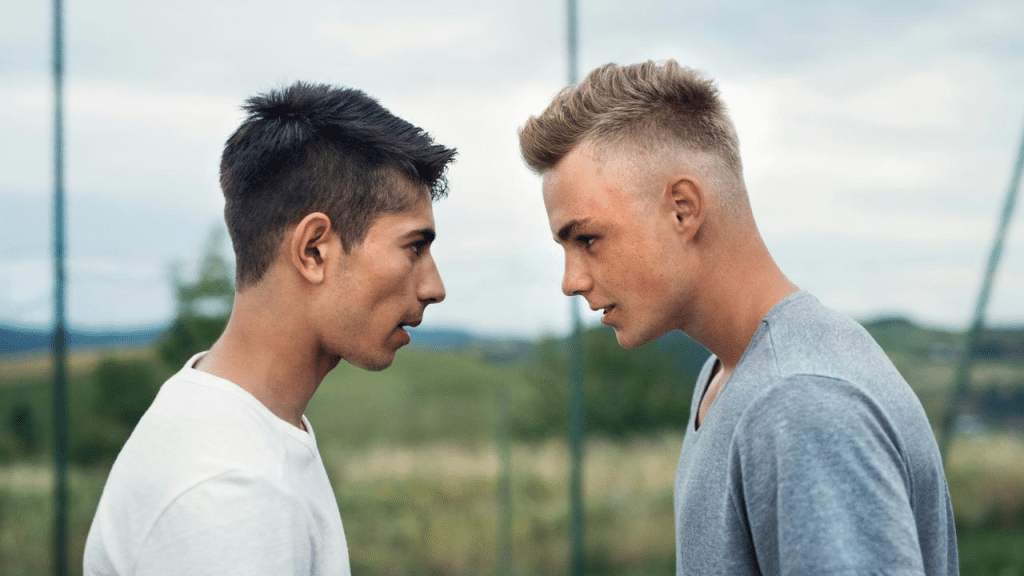 A tense standoff between two young men facing each other outdoors.