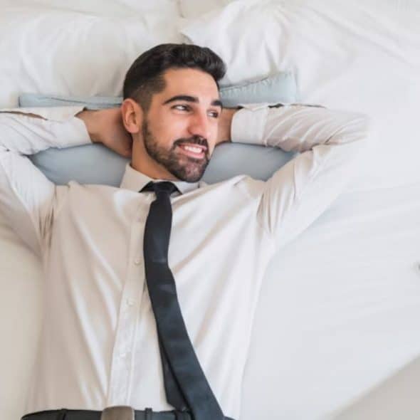 A man lying on a bed, looking contemplative with natural light coming in from the window
