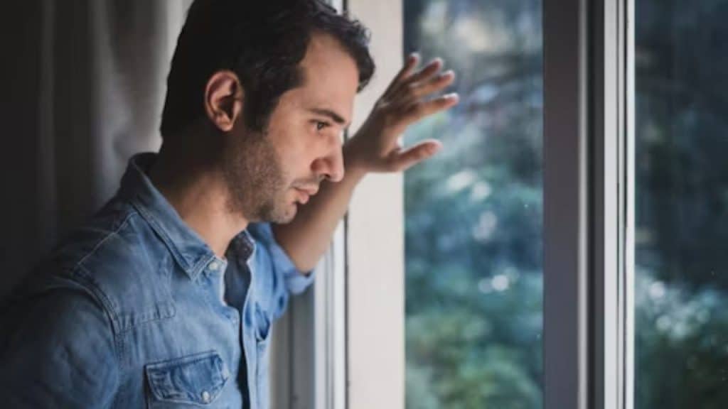 Man standing near the window of a house at night, looking protective and alert