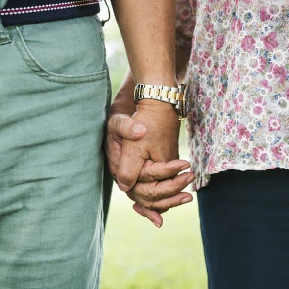 A close-up of two people holding hands outdoors.