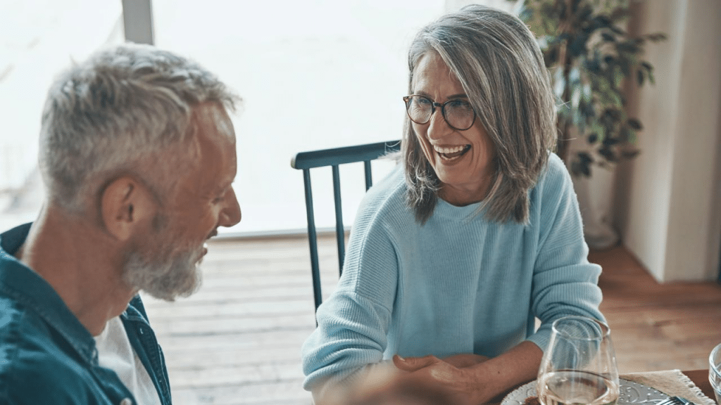 An older couple smiling and talking at a dining table.