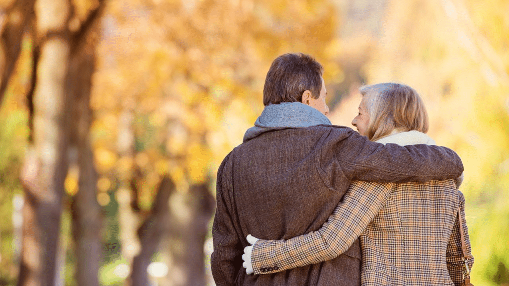An older couple walking arm in arm through a park in autumn.