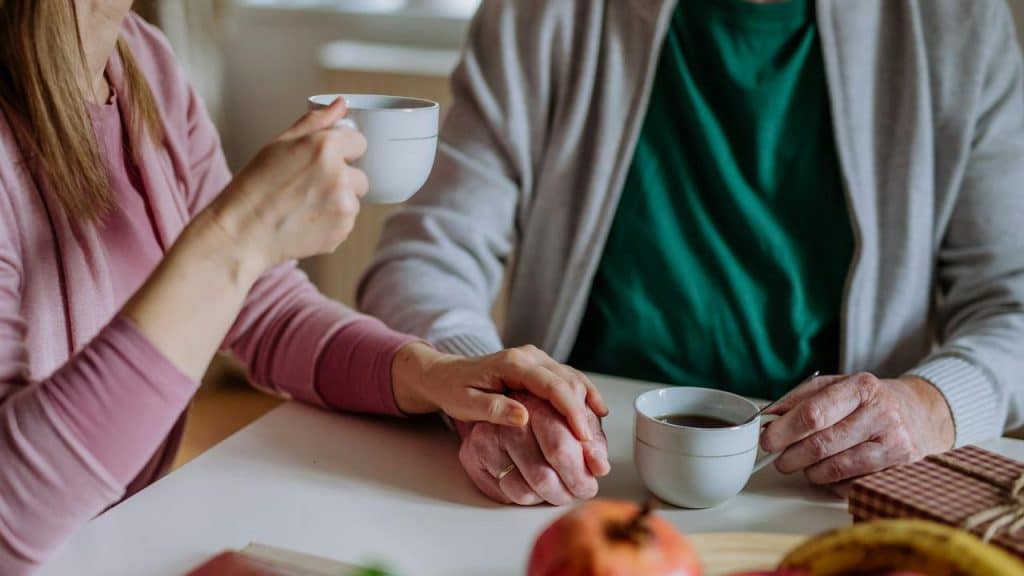 An elderly couple holds hands while having coffee together.