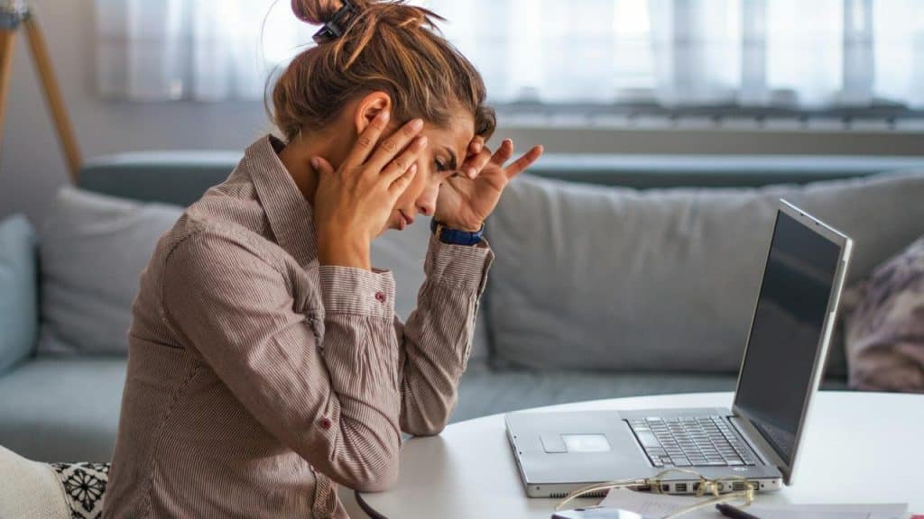 A woman holds her head in frustration while working on a laptop.