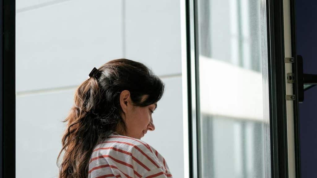 A woman stands by an open window looking down.