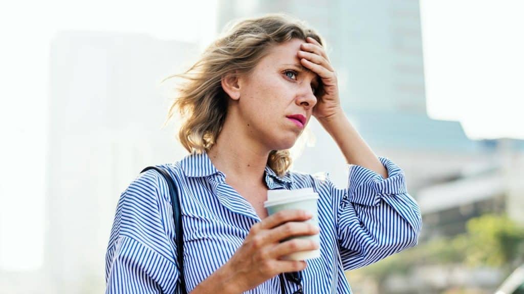 A woman looks stressed while holding a coffee cup outdoors.