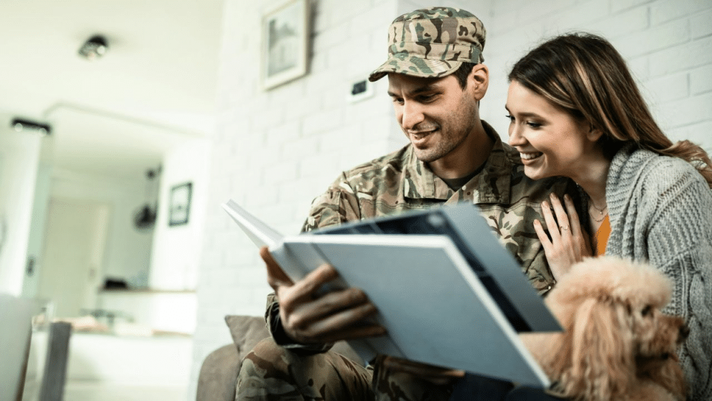 A happy soldier in camouflage and a woman look at a photo album with a dog.