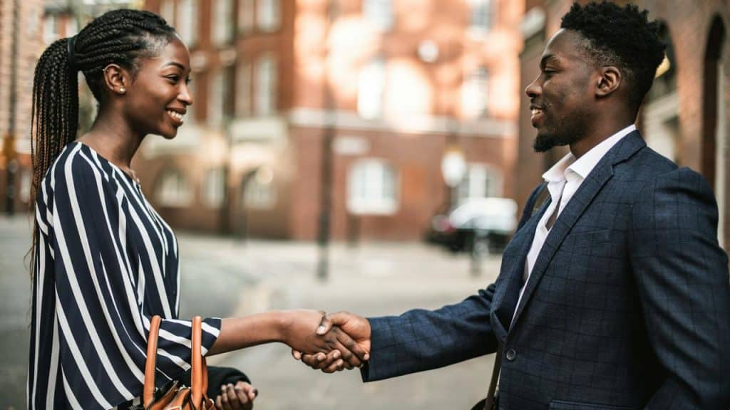 A man and woman shaking hands on a city street.