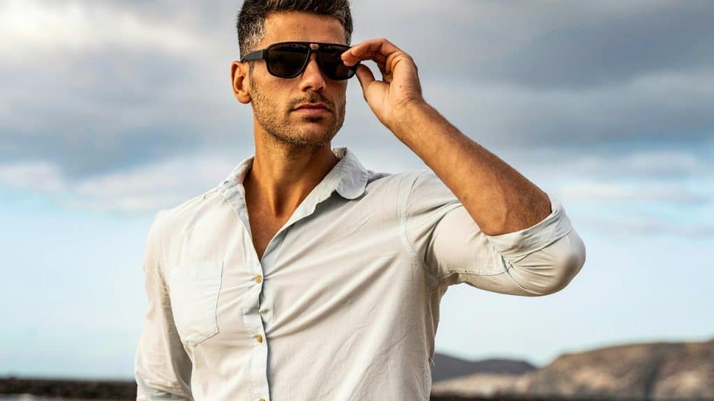 A man wearing sunglasses and a light shirt outdoors.
