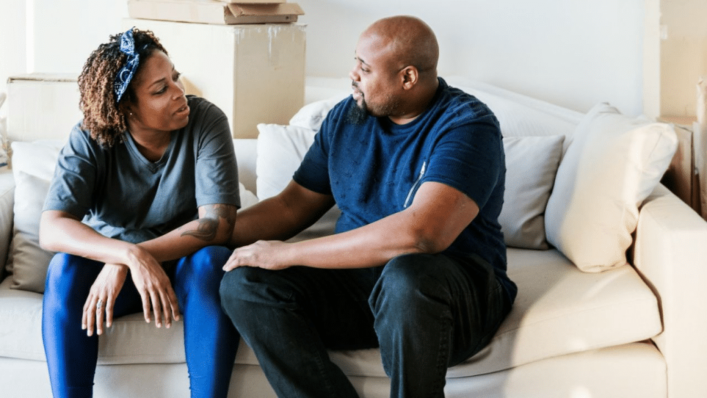 A concerned woman and a man sit on a couch and have a serious discussion in a room.