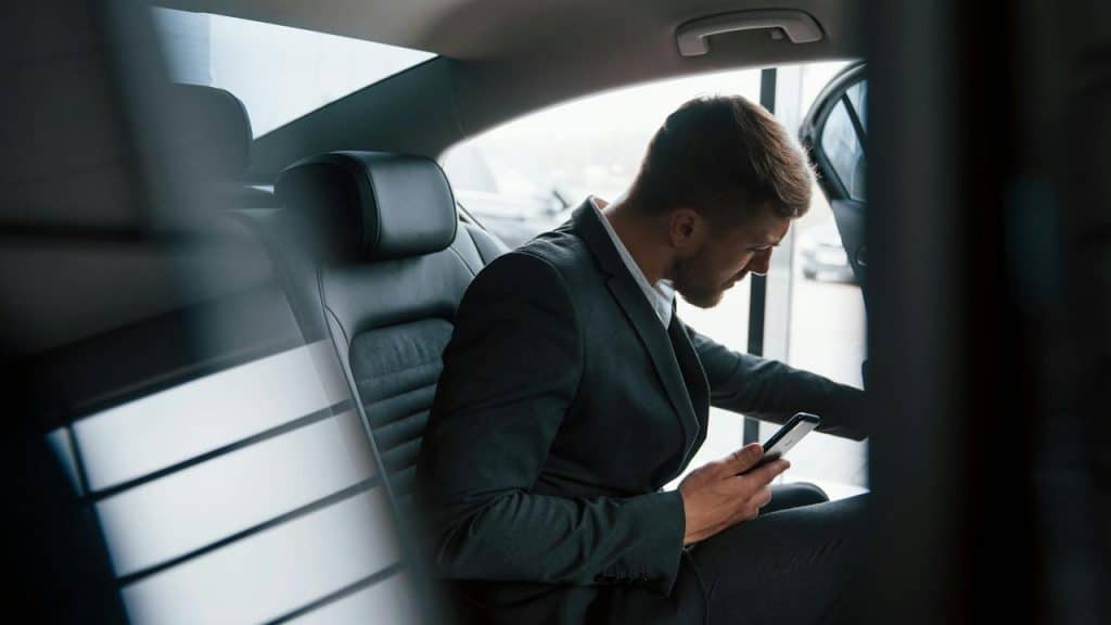 A man in a suit sitting in a car holding a phone.