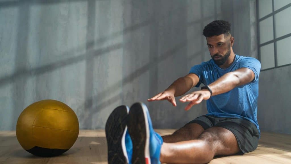 A man stretching on the floor near a yellow medicine ball.