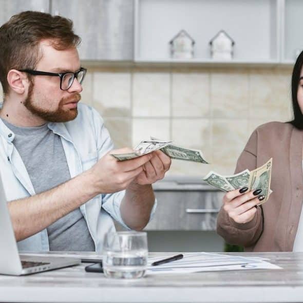A man and woman sit at a table holding money and looking at each other.
