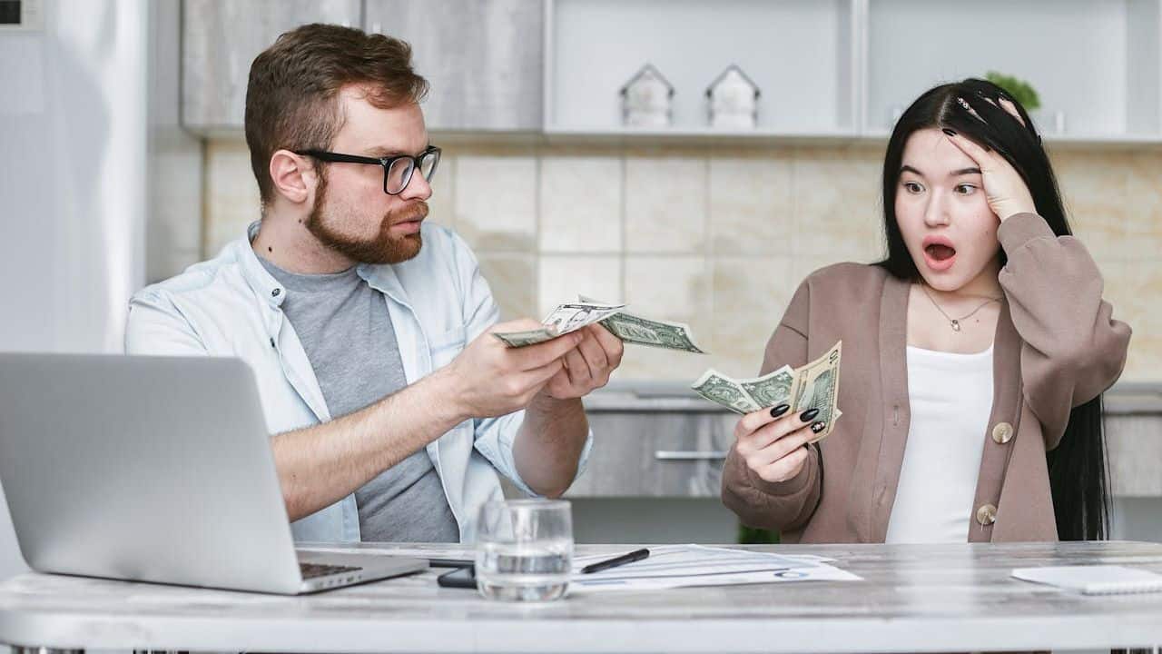 A man and woman sit at a table holding money and looking at each other.