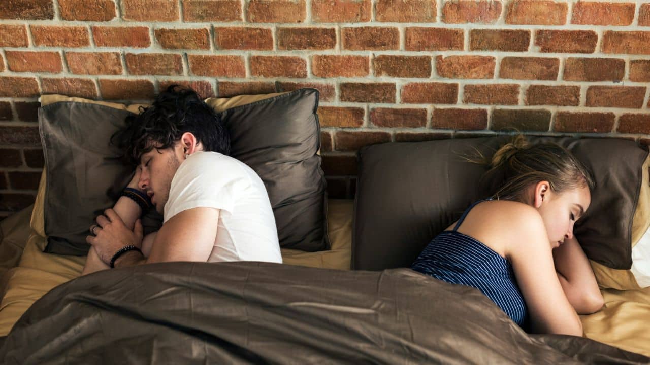 A man and a woman lie in bed back-to-back, facing away from each other.