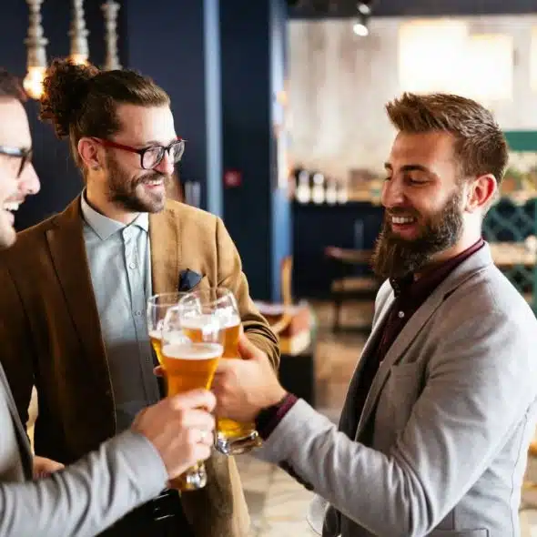 A smiling group of three men in suits celebrating with a toast and glasses of beer.