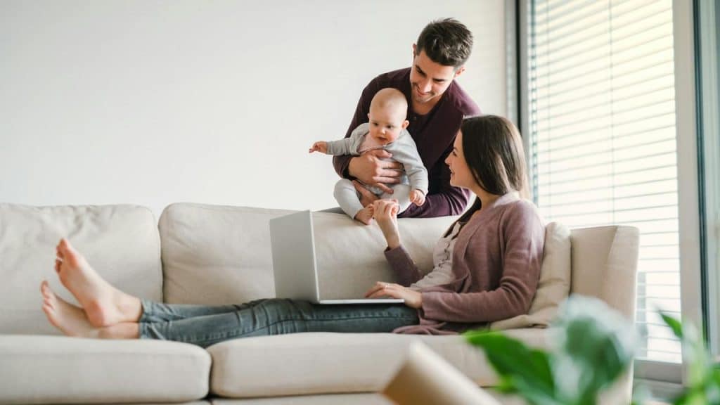 A couple at home with their baby, sitting on a couch together.